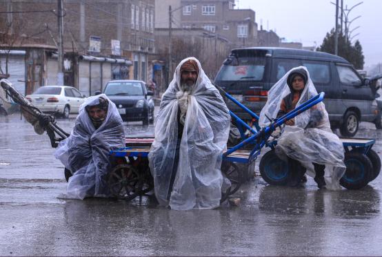 မတ် ၁၂ ရက်က ဟီရတ်ပြည်နယ် ဟီရတ်မြို့တော်ရှိ မိုးရွာနေသည့် လမ်းပေါ်တွင် ပလပ်စတစ်အစများကို ခြုံထားသည့် အာဖဂန်အလုပ်သမားများကို တွေ့ရစဉ်(Photo:AFP)
