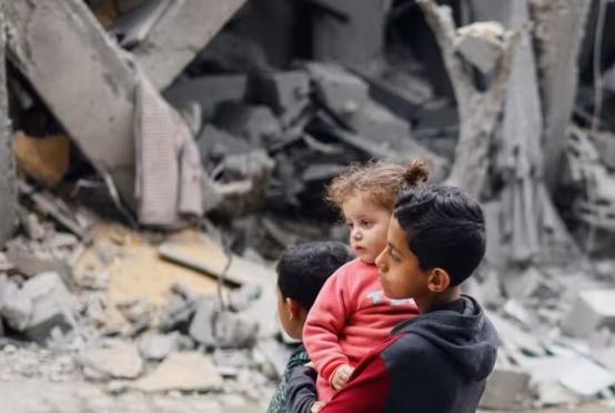အစ္စရေးတိုက်ခိုက်မှုကြောင့် ပျက်စီးနေသည့် အဆောက်အအုံအနီးတွင် ပါလက်စတိုင်းကလေးများ ရပ်နေပုံကို မတ် ၂၄ ရက်တွင် တွေ့ရစဉ်(photo: Reuters)