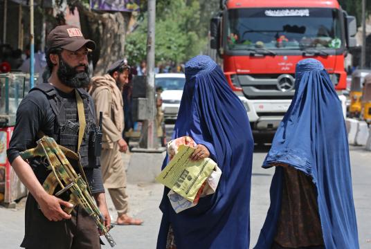 ဧပြီ ၃၀ ရက်က အာဖဂန်နစ္စတန်နိုင်ငံ ဂျာလာလာဘတ်မြို့ရှိ လမ်းတစ်နေရာတွင် တာလီဘန်လုံခြုံရေးတစ်ဦးအနီးမှ ဖြတ်သန်းသွားလာနေသောအမျိုးသမီးများကို တွေ့ရစဉ် (Photo – AFP)