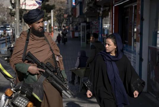 ၂၀၂၂ ခုနှစ် ဒီဇင်ဘာ ၂၆ ရက်က အာဖဂန်နစ္စတန်နိုင်ငံ ကဘူးမြို့တော်၌ တာလီဘန်လက်နက်ကိုင်တစ်ဦးအနီးတွင် လမ်းလျှောက်နေသည့် အမျိုးသမီးတစ်ဦးကို တွေ့ရစဉ် (Photo: AP)