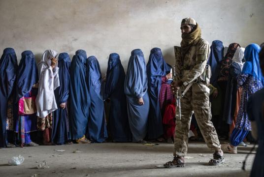 မေ ၂၃ ရက်က အာဖဂန်နစ္စတန်နိုင်ငံ ကဘူးမြို့တော်တွင် အကူအညီပေးရေးအဖွဲ့တစ်ဖွဲ့က ဖြန့်ဝေပေးနေသည့် အစားအစာများကို ရယူရန် တန်းစီစောင့်ဆိုင်းနေသည့် အမျိုးသမီးများအနီးတွင် တာလီဘန် လက်နက်ကိုင်တစ်ဦးကို တွေ့ရစဉ် (Photo – AFP)