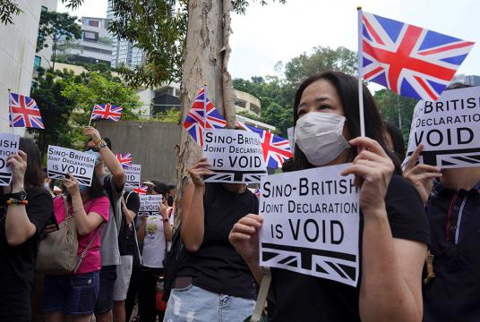 စက်တင်ဘာ ၁၅ ရက်က ဟောင်ကောင်မြို့ ဗြိတိန်ကောင်စစ်ဝန်ရုံးအပြင်ဘက်တွင် စာတန်းများနှင့် ဗြိတိန်အလံများကို ဆန္ဒပြသူများက ကိုင်ဆောင်ထားစဉ် (Photo: AP)