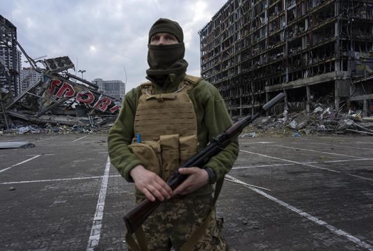 မတ် ၃၀ ရက်တွင် စစ်သားတစ်ဦး  ကိယက်ဗ်မြို့ရှိ ဗုံးကြဲတိုက်ခိုက်ခံရပြီးနောက် ပျက်စီးသွားသည့် ဈေးဝယ်စင်တာတစ်ခုရှေ့၌ ဓာတ်ပုံရိုက်ကူးခံနေစဉ် Photo : AP