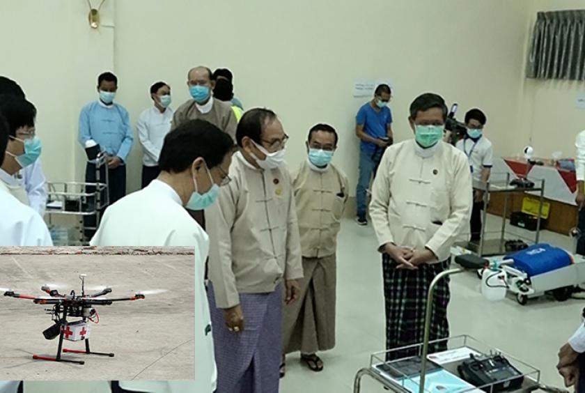  ပညာရေးဝန်ကြီးဌာနကလှူဒါန်းသည့် Trolley Robot များကို တာဝန်ရှိသူများက ကြည့်ရှုနေစဉ်(ပုံကြီး) အသံချဲ့စက်ပါဝင်သော Drone (ပုံသေး) အား တွေ့ရစဉ်